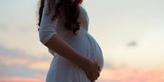 A pregnant woman in a white dress stands outdoors, embodying prenatal health and wellness, aligning with WeNatal's focus on prenatal supplements and support.